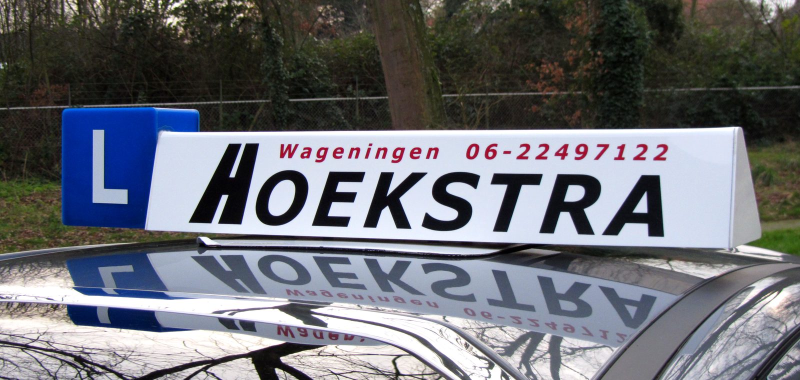Het daklicht van de lesauto van Autorijschool Hoekstra met het blauwe L-bord en de tekst Hoekstra Wageningen